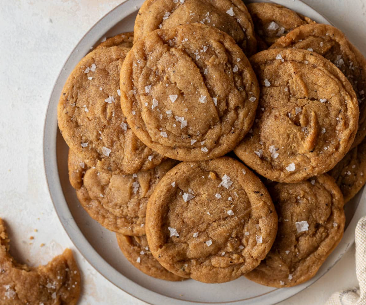 A neat stack of thick, golden-brown chocolate chipless cookies with rippled, crinkly edges and a soft, chewy center on a wire cooling rack.