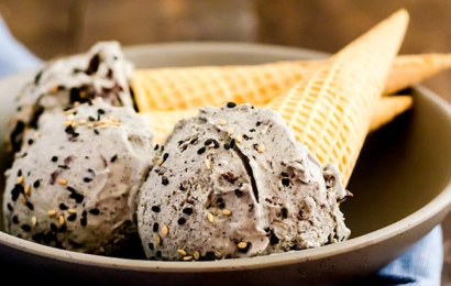 A scoop of creamy, smooth homemade vanilla bean ice cream being pulled from a metal loaf pan with a vintage metal ice cream scoop