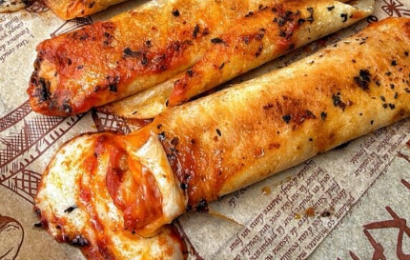 A platter of golden-brown, crispy pizza roll ups made with crescent dough, oozing with melted mozzarella cheese and pepperoni slices, served with a bowl of warm marinara sauce.